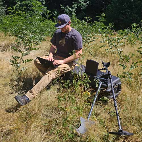 Man using a metal detector in a grassy outdoor setting